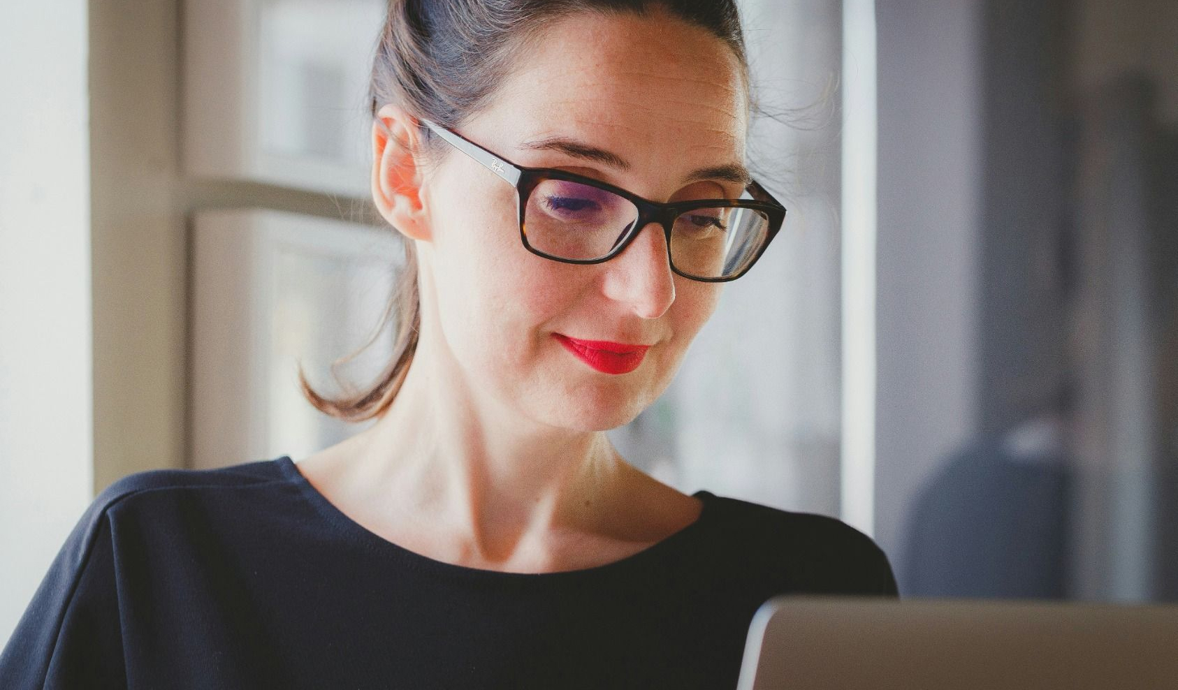 A woman looks thoughtfully at her laptop while typing