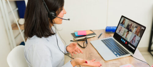 A woman wearing a headset speaks to a group of people in an online video conference meeting