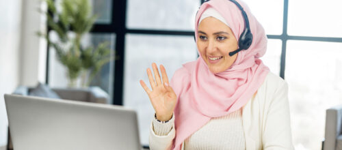 A woman wearing a headset waves to someone she is having a video meeting with