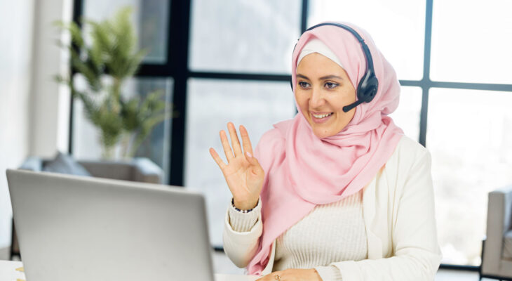 A woman wearing a headset waves to someone she is having a video meeting with