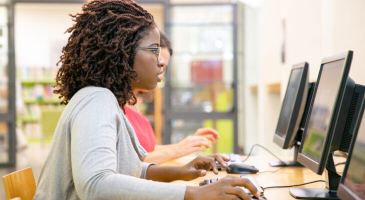 A row of people sit at publicly available desktop computers