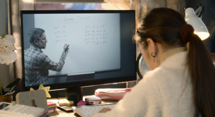 A student watches a professor on a computer screen and takes notes