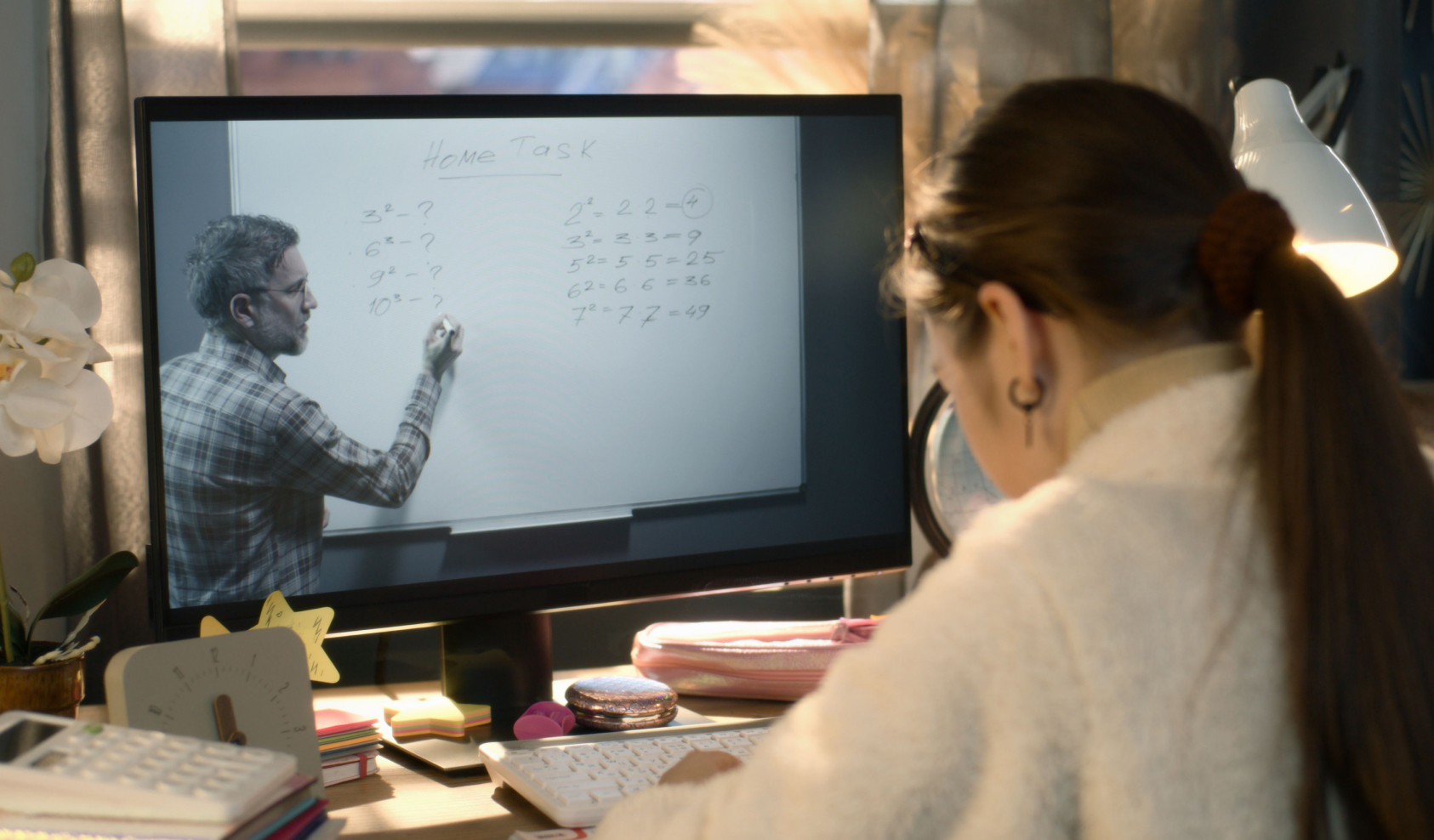 A student watches a professor on a computer screen and takes notes