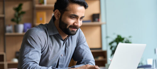 A man smiles while working on his laptop