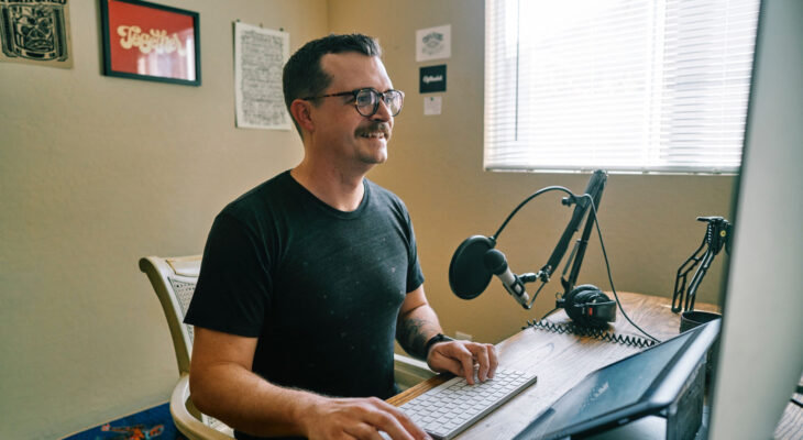 A man with a home recording studio smiles as he works on his computer