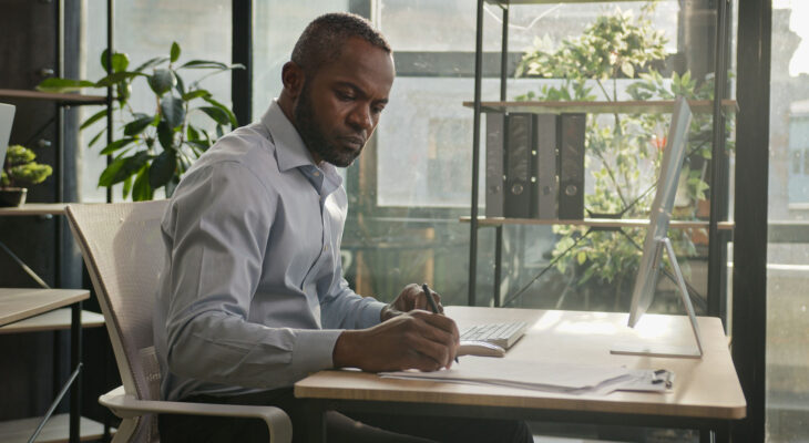 A man sitting at a desk writes on a piece of paper