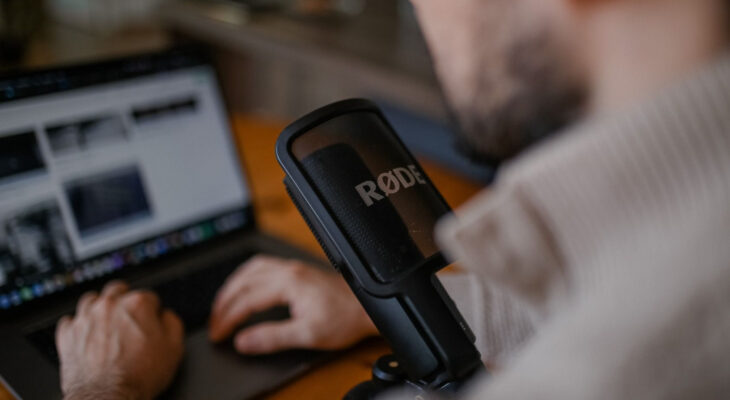 A man with a professional microphone in front of him uses his laptop