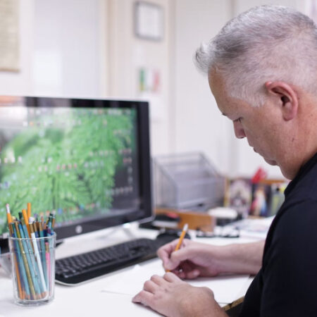 A man sits at a desk and draws on a piece of paper
