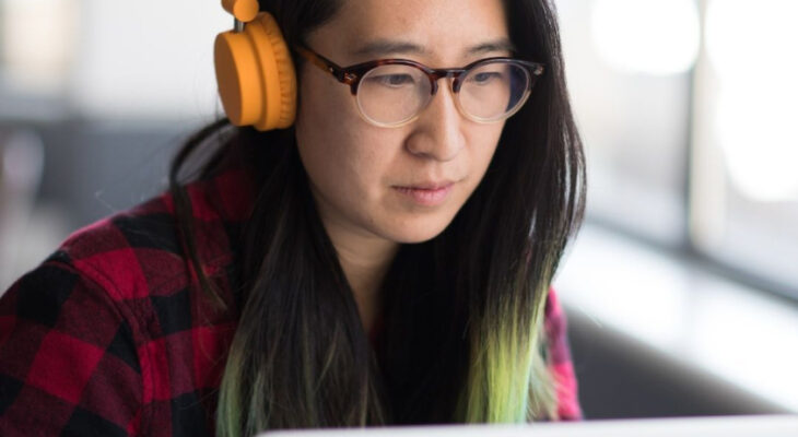 A woman wearing headphones works on a laptop in an office