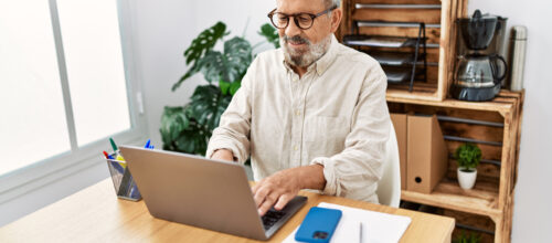 A man sits at his desk and types on his laptop