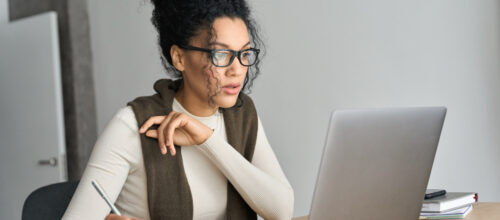 A woman reads on her laptop and takes notes