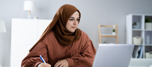 A woman takes notes while watching a video on her laptop
