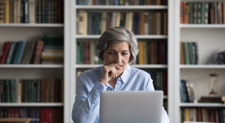 A professor sits in a library looking at her laptop