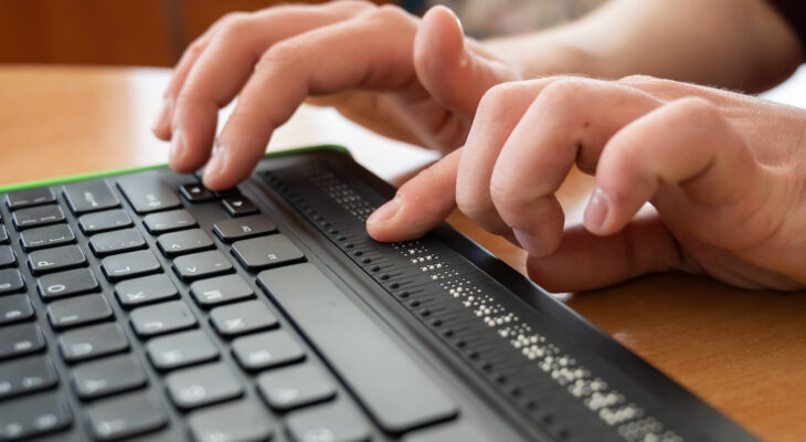 A blind man uses a computer with a Braille display and a computer keyboard. Inclusive device.