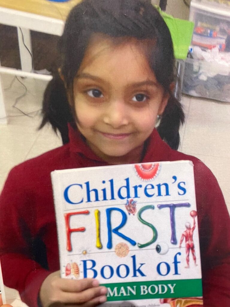 A young girl holds a book titled Children's First Book of Human Body.