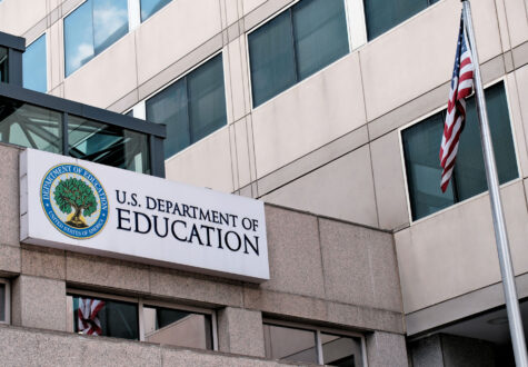 Exterior sign of the U.S. Department of Education building with its seal and a U.S. flag on a pole in the foreground.