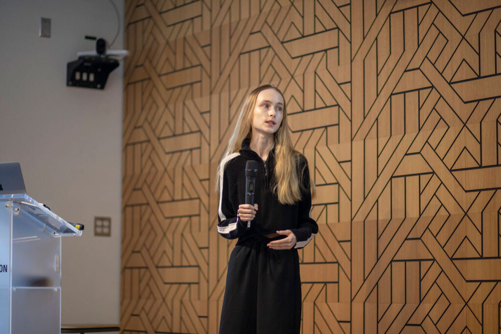 A young woman wearing a black top and pants gives a presentation.