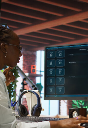 Person with long braids and a white shirt works at a desktop computer displaying a generative AI prompt screen.