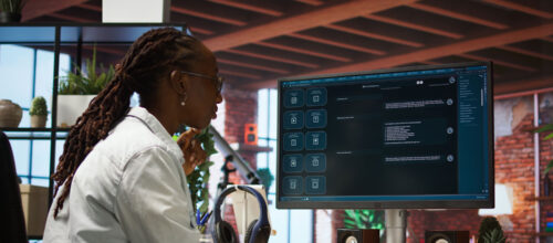 Person with long braids and a white shirt works at a desktop computer displaying a generative AI prompt screen.