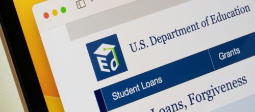 A close-up, angled view of a computer screen displaying the U.S. Department of Education website. The navigation bar highlights "Student Loans," with "Grants" visible beside it and the page heading beginning with "Student Loans, Forgiveness."