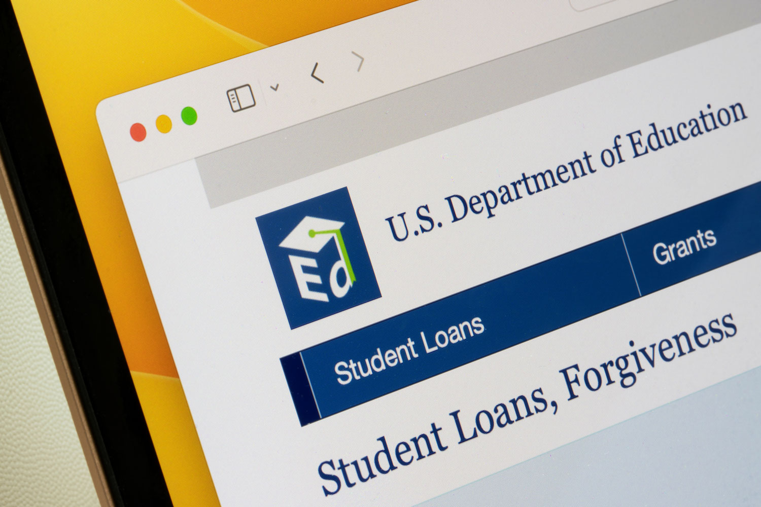 A close-up, angled view of a computer screen displaying the U.S. Department of Education website. The navigation bar highlights "Student Loans," with "Grants" visible beside it and the page heading beginning with "Student Loans, Forgiveness."